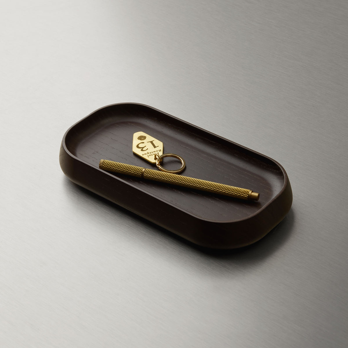 Decor Walther ONYO AS Ablageschale aus dunklem Eschenholz mit natürlicher Holzmaserung, dekoriert mit goldenem Schlüsselanhänger und Stift als stilvolle Aufbewahrung für kleine Alltagsgegenstände, Artikelnummer 0691190
