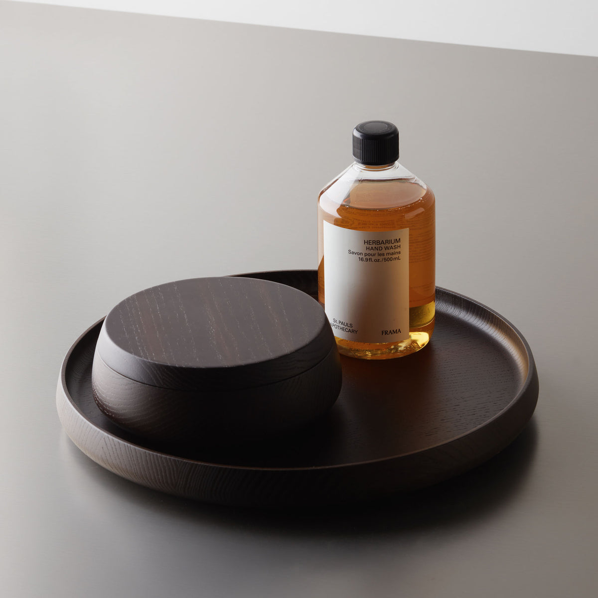 Rundes Dekotablett Decor Walther ONYO aus dunklem Eschenholz, arrangiert mit einer passenden Aufbewahrungsdose aus Holz und einer Pflegeflasche