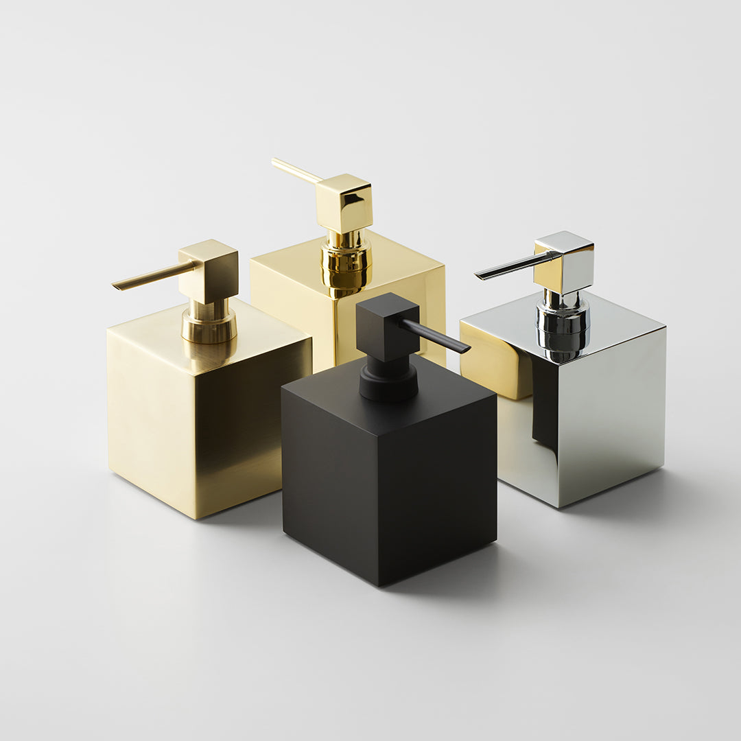 Vier freistehende Seifenspender DW475 von Decor Walther in den Oberflächen Chrom, Schwarz-matt, Gold 24 Kt. und Gold-matt auf hellem Untergrund als stilvolle Gruppenaufnahme.