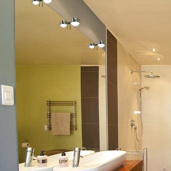 Stilvolles Badezimmer mit PUK Mini Fix Plus Lampen in Chrom montiert über einem Spiegel. Die modernen Leuchten sorgen für eine klare, warmweiße Beleuchtung, die das elegante Interieur hervorhebt, mit einer Dusche und einem Handtuchhalter im Hintergrund.