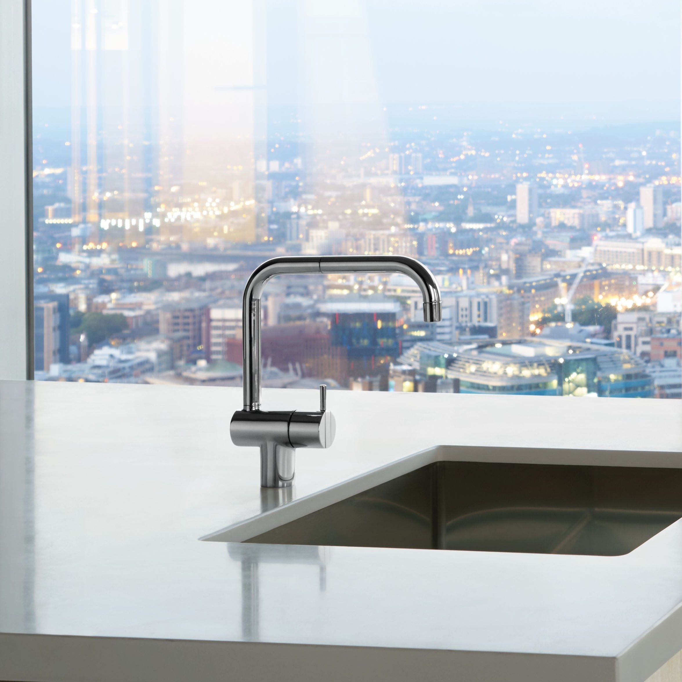 Ein moderner, verchromter Wasserhahn der Marke Vola KV1 ist auf einer Küchentheke montiert, mit einem Panoramablick auf eine Stadtlandschaft im Hintergrund.