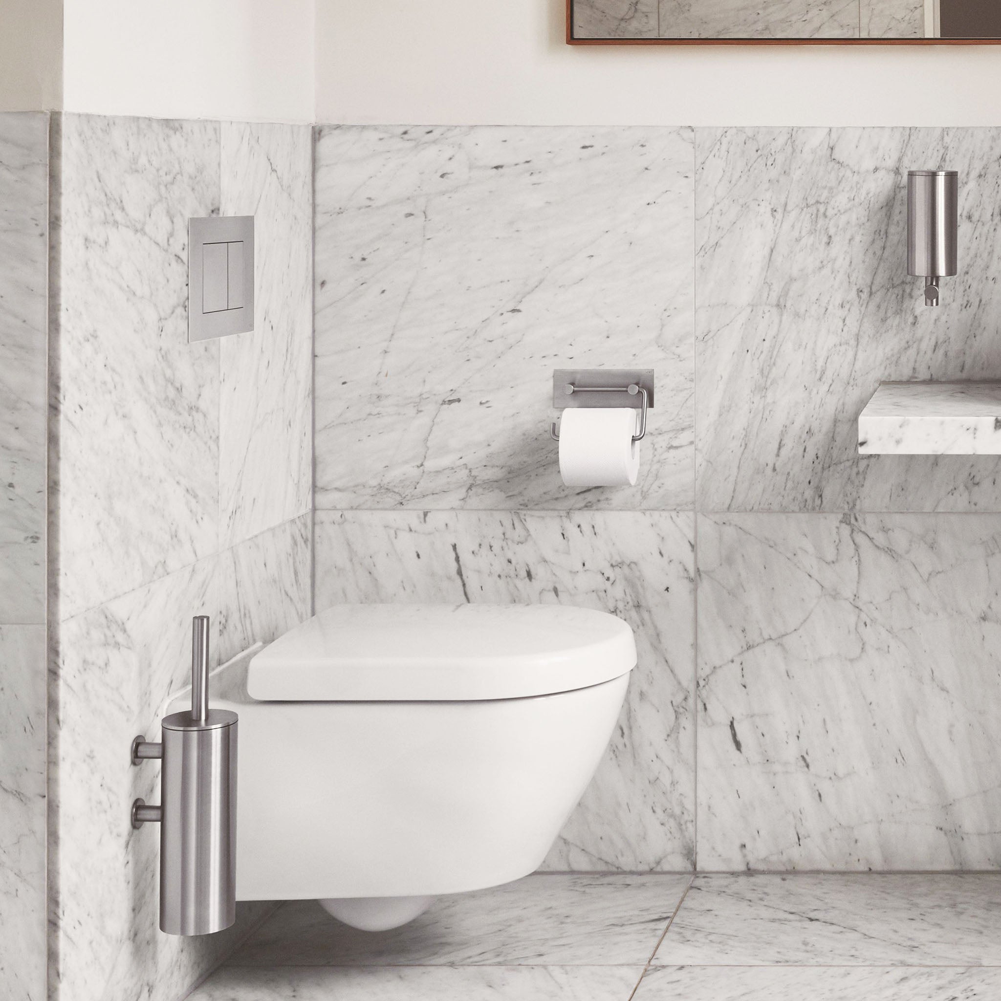 Vola Badzubehör in Edelstahl gebürsteter Oberfläche. Eine WC Bürste, ein Seifenspender, eine Toilette, Drückerplatte und der Toilettenpapierhalter.