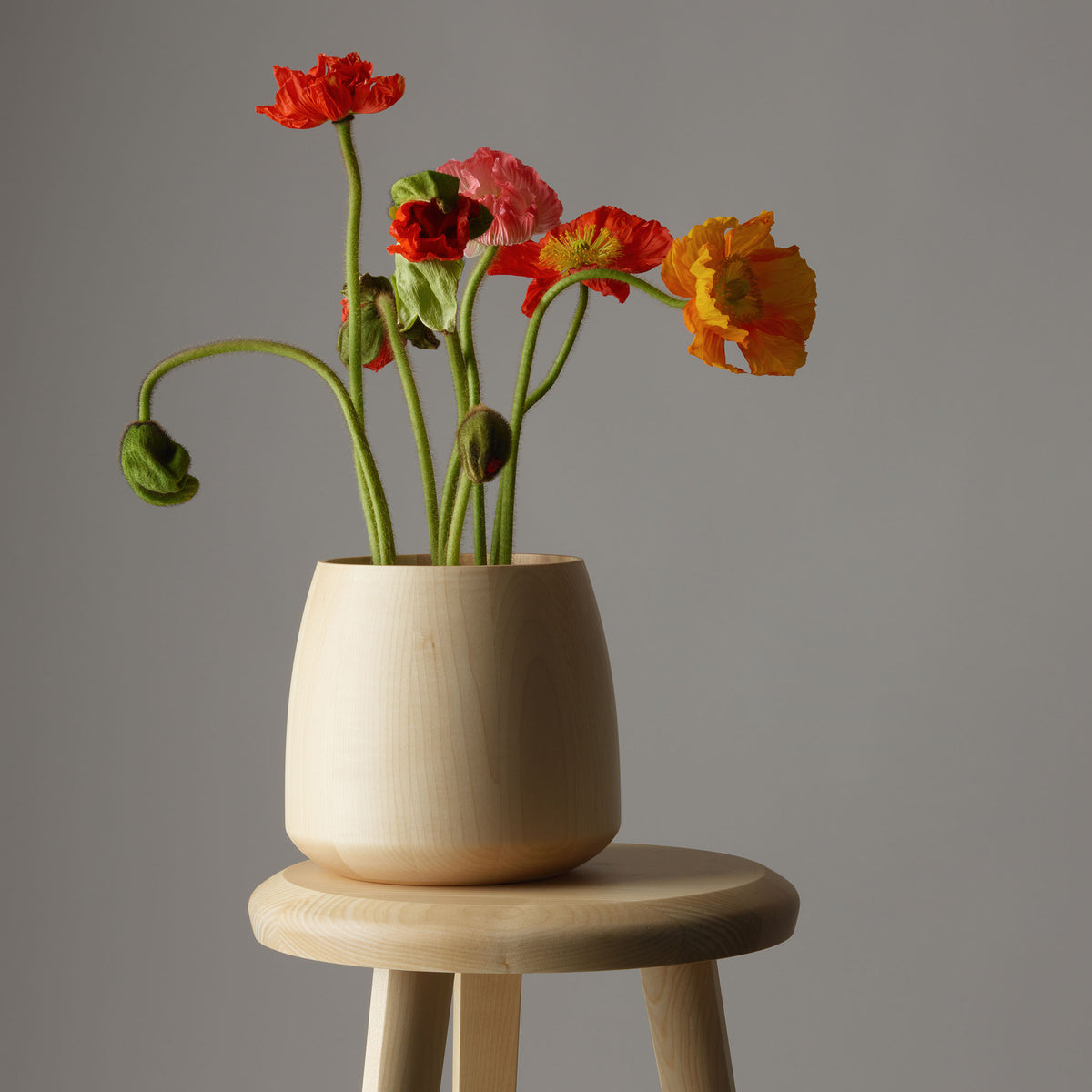 Decor Walther ONYO Blumenvase aus natürlichem Ahornholz mit bunten Mohnblumen, dekorativ auf einem passenden Holzhocker der ONYO Kollektion arrangiert