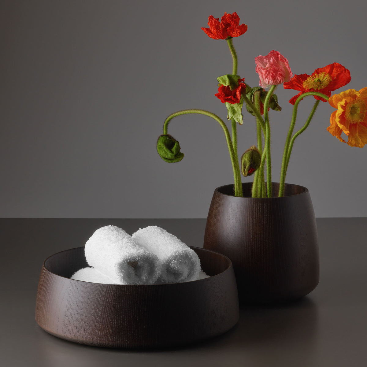 Decor Walther ONYO Holzvase aus dunklem Eschenholz mit farbenfrohen Mohnblumen, kombiniert mit einer passenden Holzschale und gerollten Gästehandtüchern