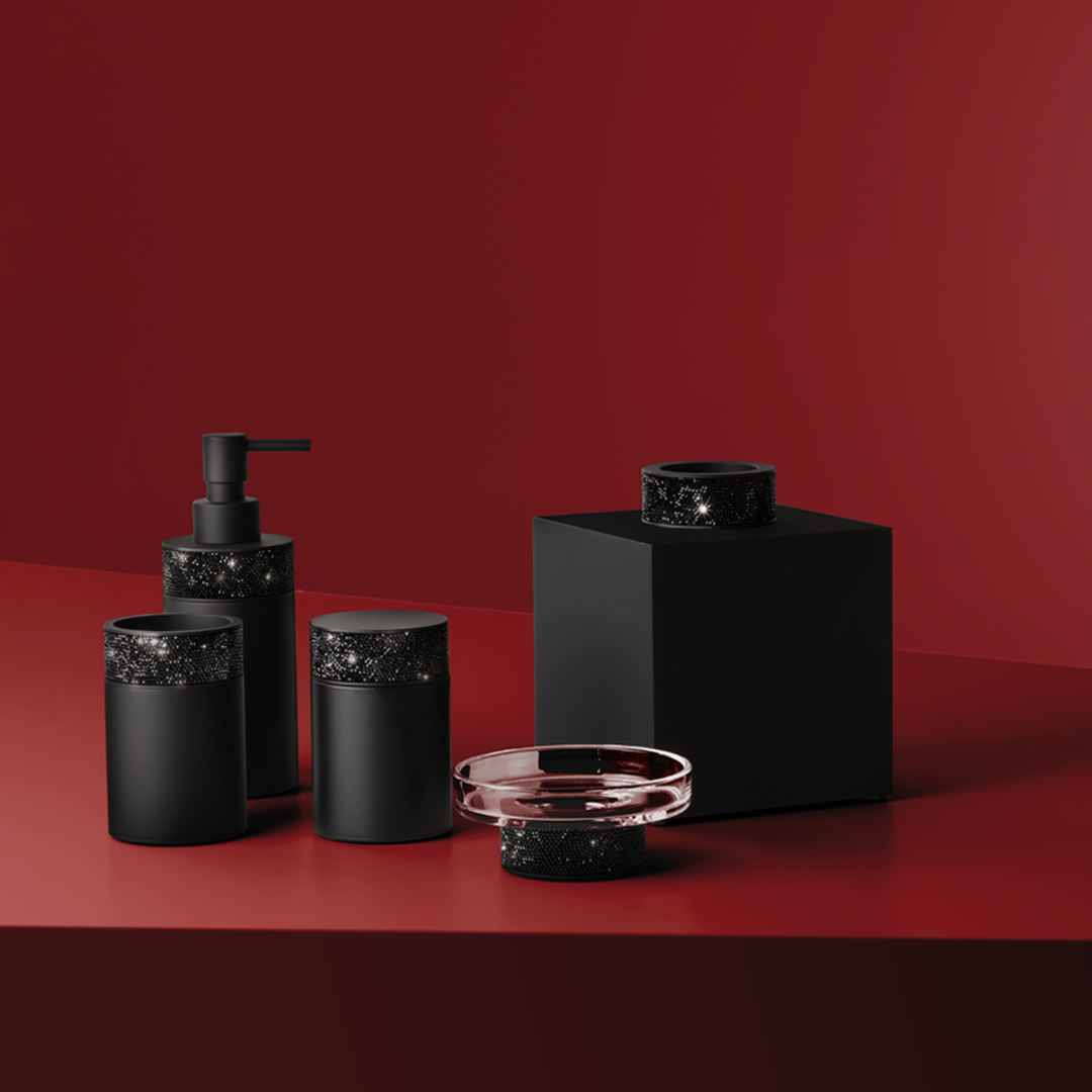 Decor Walther Rocks Accessoires in Schwarz matt mit schwarzem Swarovski-Kristallbesatz – Seifenspender, Dosen und Kristallglas-Seifenschale vor tiefrotem Hintergrund.