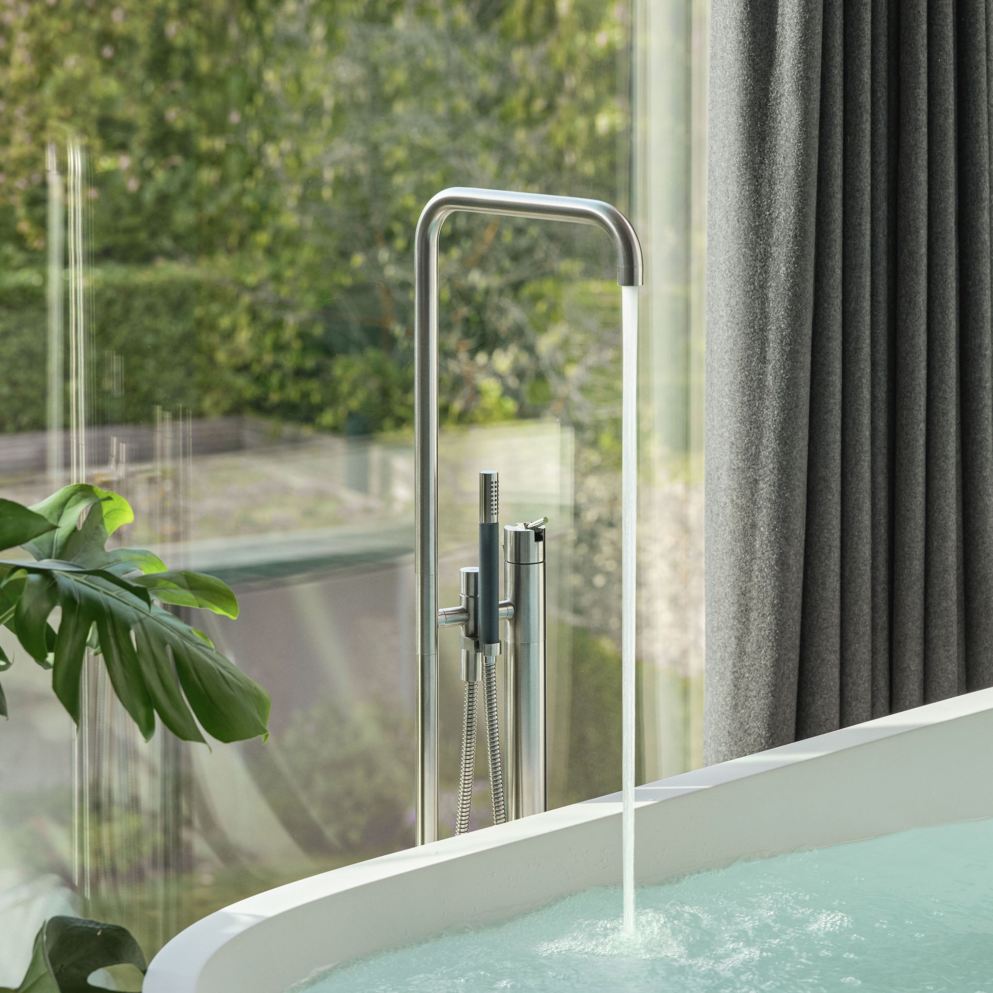 Freistehende Vola FS1 Bodenarmatur aus gebürstetem Edelstahl, mit Auslauf und Stabhandbrause.